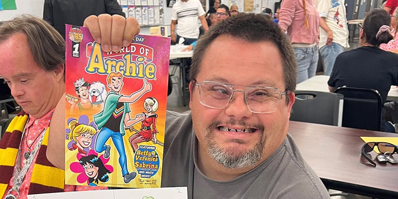 Man smiling holding Archie comic book at community event in Ventura County.